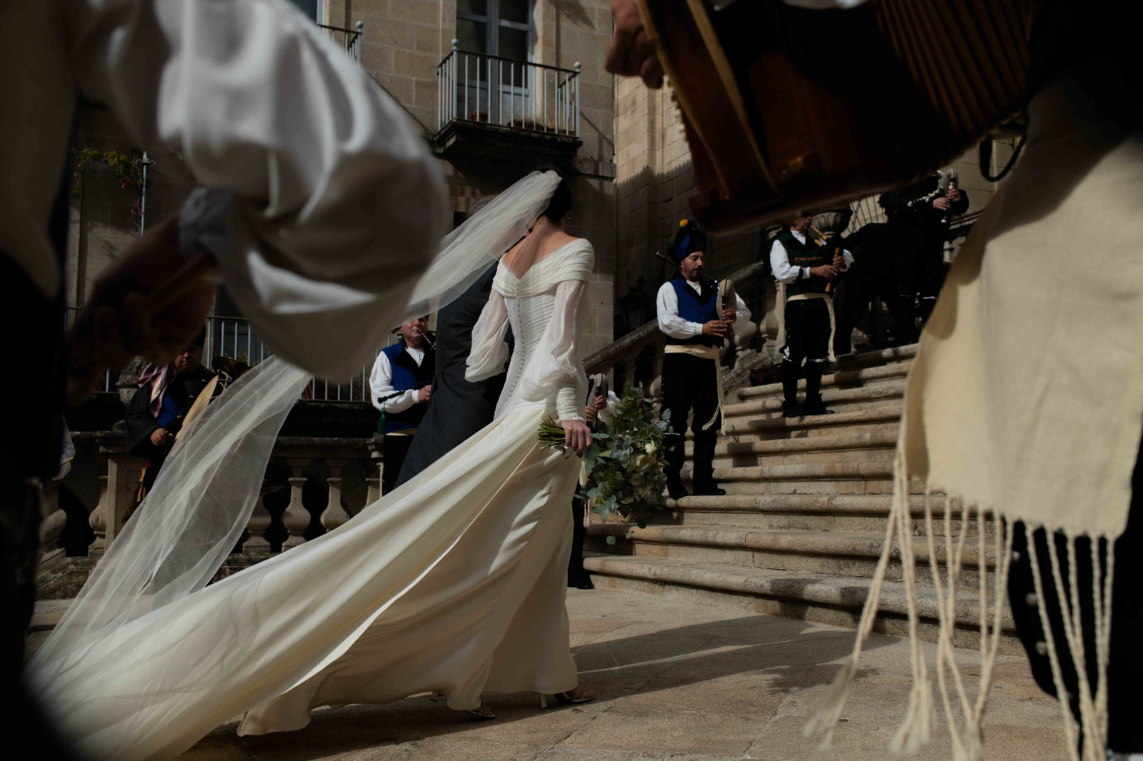 Novia con vestido largo y velo caminando junto a músicos tradicionales durante una boda en Galicia