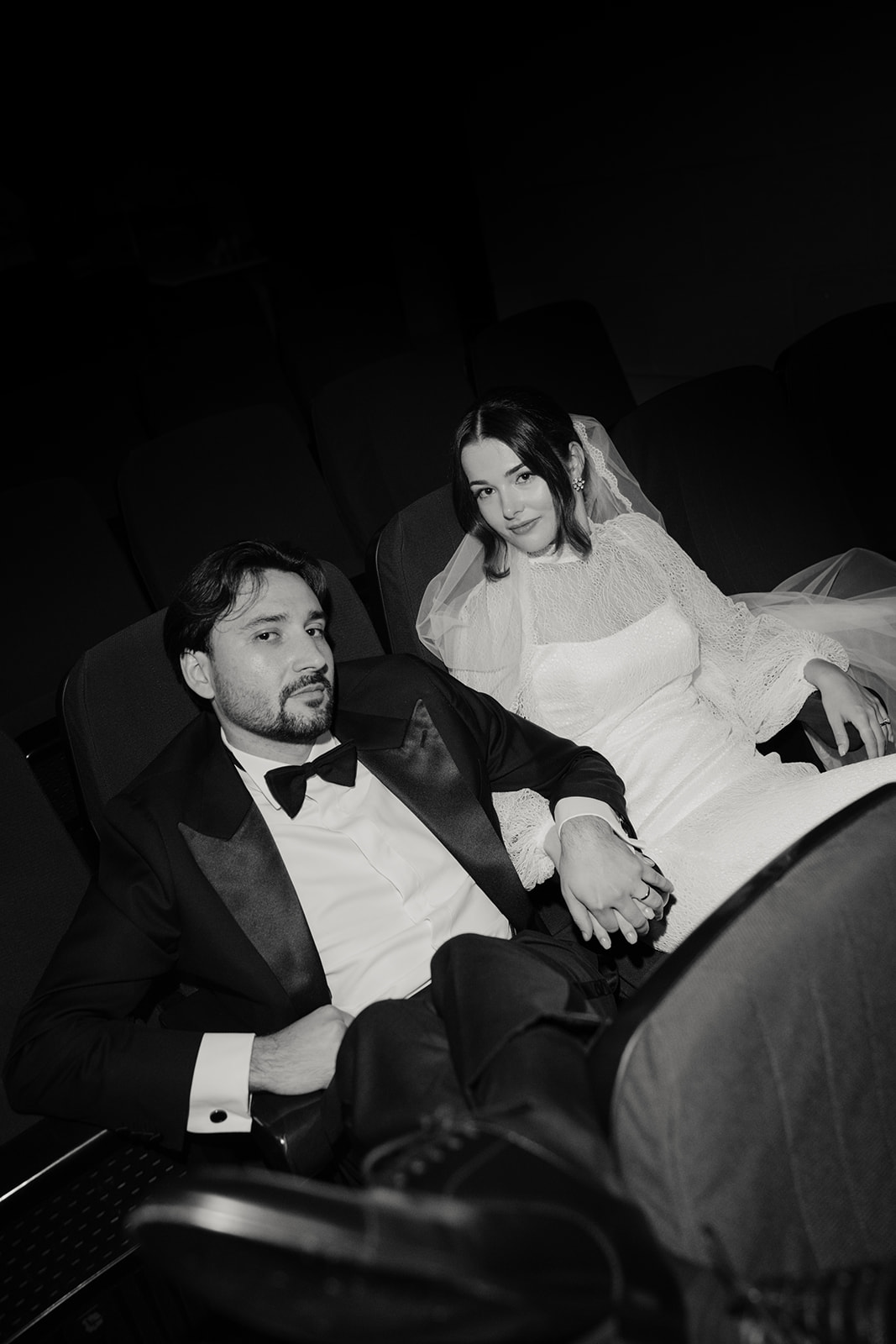 Sofía y Andrew sentados en un cine, vestidos de novios y cogidos de la mano, en una fotografía en blanco y negro.