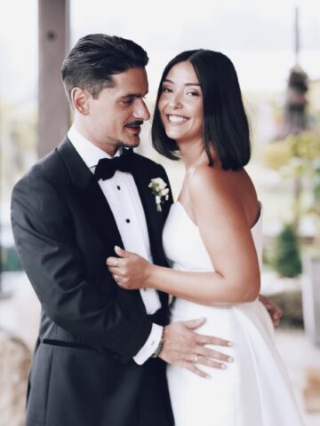 Alejandra & Rubén | Retrato de boda en Galicia en bodegas Lagar de Pintos Alejandra sonríe a cámara mientras Rubén la abraza, vestidos de novia y esmoquin durante su boda en Galicia.