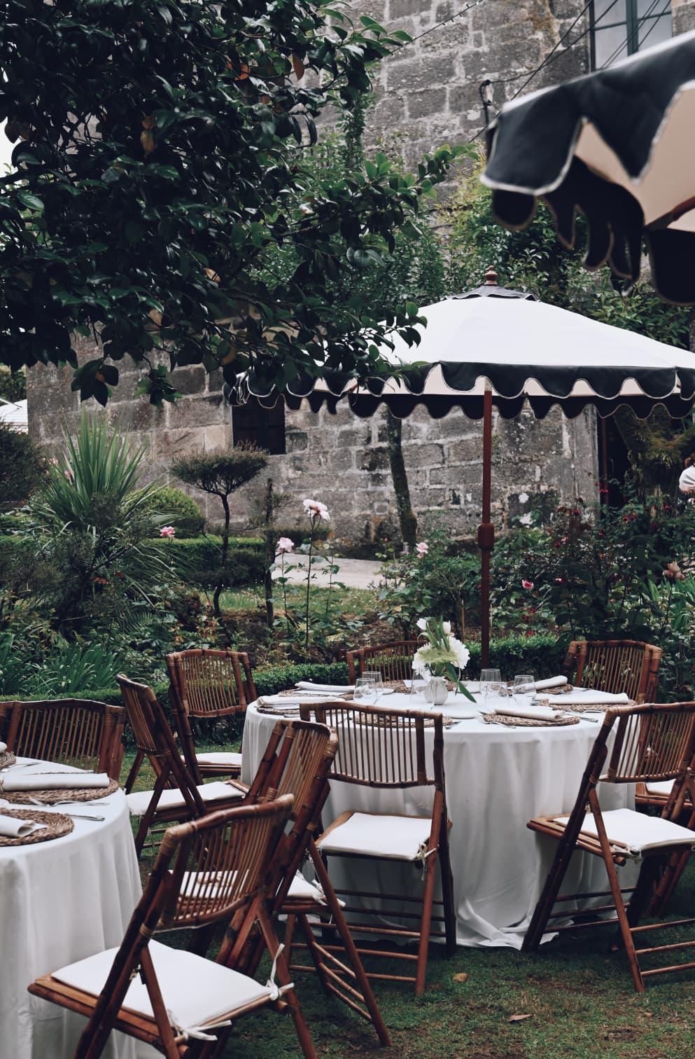 Mesas de boda en el jardín del Pazo de San Lorenzo, con sillas de madera, mantelería blanca y sombrillas.