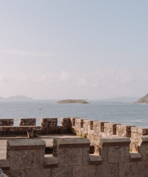 Costa de Galicia - Parador de Baiona | Galicia Experiences | MINIMÚ ATELIER Parador de Baiona Vista de la costa gallega desde una fortaleza de piedra con el mar y las islas al fondo