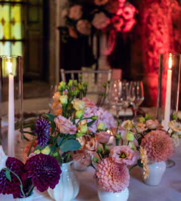 Julia & Aidan | Centros florales y velas del banquete Centros de mesa con dalias rosas y granates, flores en pequeños jarrones blancos y velas encendidas durante el banquete de Julia y Aidan.