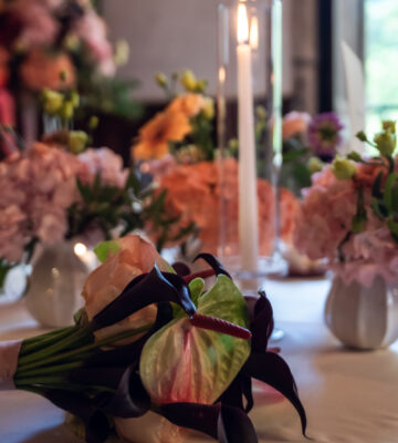 Julia & Aidan | Ramo de novia y decoración floral Ramo de novia de Julia con anturios verdes y flores oscuras, sobre una mesa decorada con arreglos florales y velas.