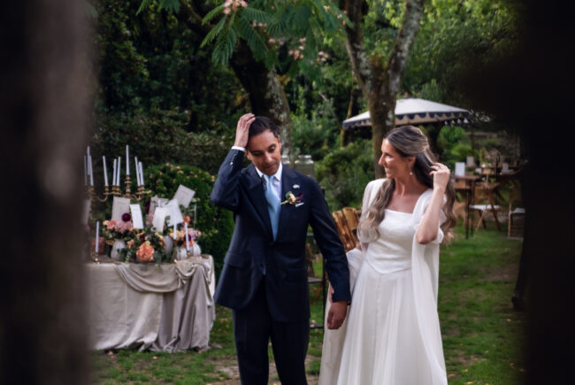 Julia & Aidan | Cóctel de boda en Galicia pazo San Lorenzo Julia y Aidan pasean de la mano durante el cóctel de su boda en un jardín de Galicia, junto a una mesa con flores y velas.