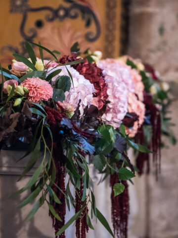 Julia & Aidan | Decoración floral de la ceremonia Arreglo floral de ceremonia con hortensias rosas, flores granates y verdes colgantes sobre una balaustrada de piedra.