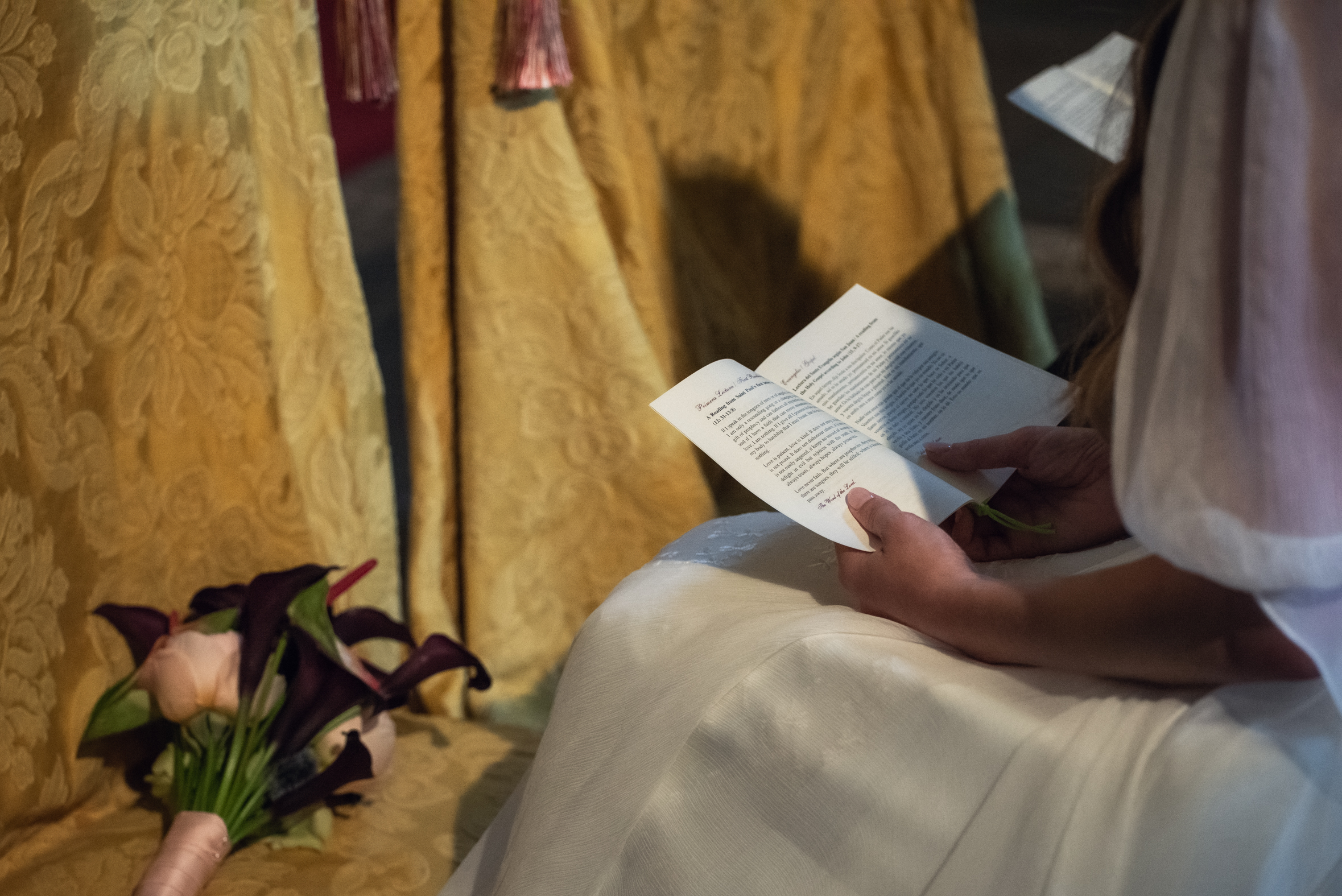 Julia sostiene el libro de la ceremonia junto a su ramo de calas oscuras y rosas claras, sentada en la iglesia.