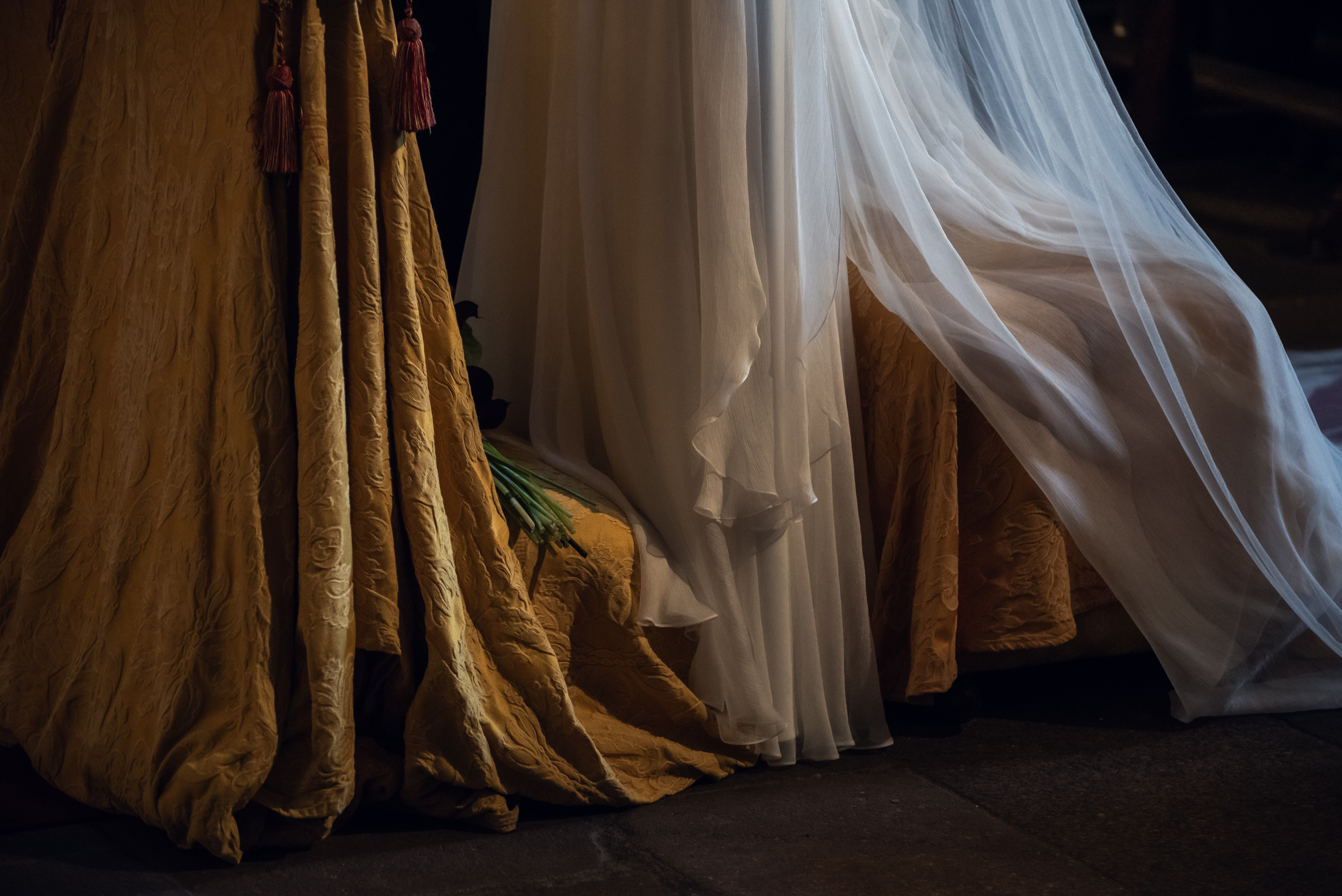 Detalle del vestido blanco y el velo de Julia junto a los tejidos dorados del interior de la iglesia durante su boda.